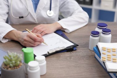 Klinikteki ahşap masada hastanın sağlık kartını dolduran doktor.