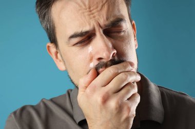 Üzgün adam açık mavi arka planda ağlıyor, yakın plan