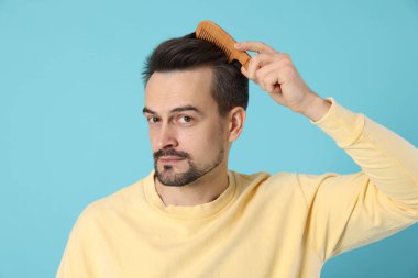Yakışıklı adam saçlarını açık mavi arka planda tarak ile tarıyor.