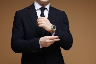 Kahverengi arka planda şık saati olan klasik takım elbiseli adam, yakın plan.