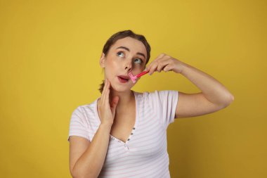 Güzel bir kadın, açık yeşil arka planda jiletle bıyığını tıraş ediyor.