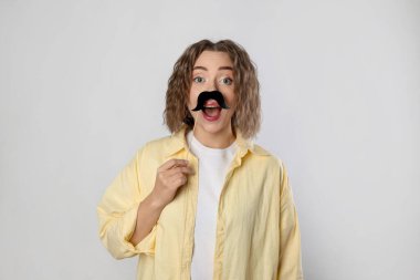 Gri arka planda sahte kağıt bıyıklı duygusal kadın.