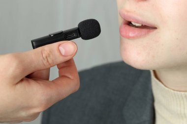 Açık gri arka planda lavalier mikrofona konuşan kadın, yakın plan.