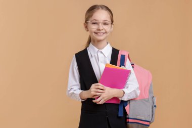 Sırt çantası ve kahverengi arka planda defterleri olan liseli kız.