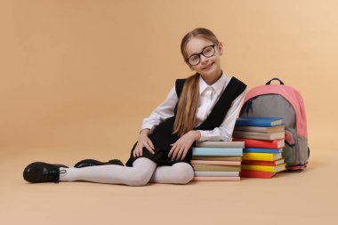 Sırt çantalı liseli kız ve kahverengi arka planda yığınla kitap.