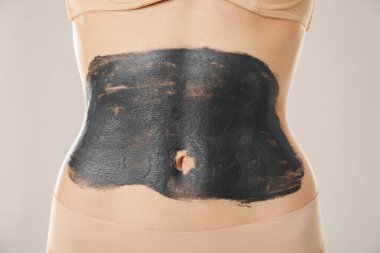 Kadın göbeğine sarılıp açık gri arka plana sarılıyor, yakın plan.