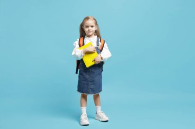 Sırt çantası ve açık mavi arka plan kitabı olan tatlı bir kız öğrenci.