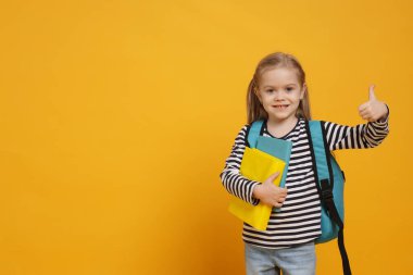 Sırt çantası ve sarı arka planda baş parmak gösteren kitapları olan tatlı bir kız öğrenci. Metin için boşluk
