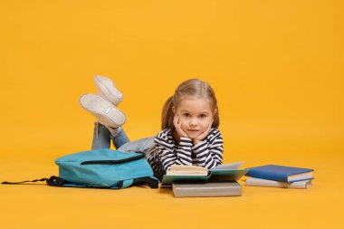 Sırt çantalı, sarı arka plan kitapları okuyan tatlı bir kız öğrenci.