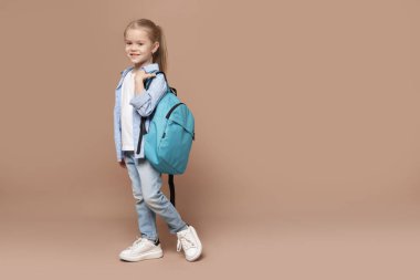 Kahverengi arka planda sırt çantası olan tatlı bir kız öğrenci. Metin için boşluk