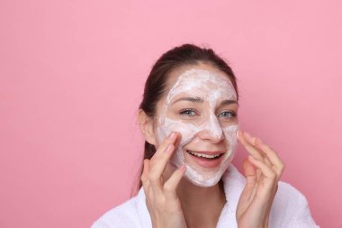 Spa günü. Güzel bir kadın pembe arka planda yüzüne maske takıyor.