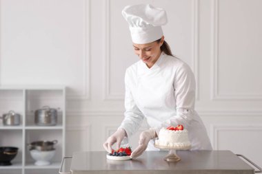 Pastacı mutfakta taze böğürtlenlerle pasta süslüyor.