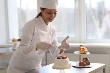 Şekerci, mutfaktaki kekin üzerine pudra şekeri serpiyor.