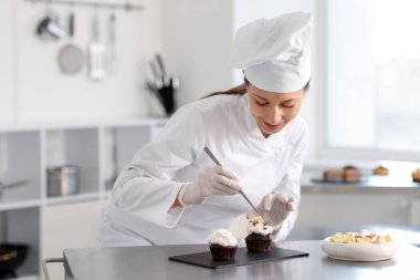 Şekerci mutfakta bir parça çikolatayla kek dekore ediyor.