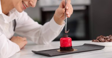 Şekerci lezzetli bir tatlıyı masada bir parça çikolatayla süslüyor, seçici odaklı.