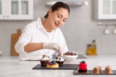 Şekerci, masada bir parça çikolatayla kek süslüyor.
