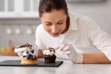 Şekerci, masada bir parça çikolatayla kek süslüyor.