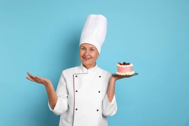 Açık mavi arka planda pastası olan profesyonel pasta şefi.