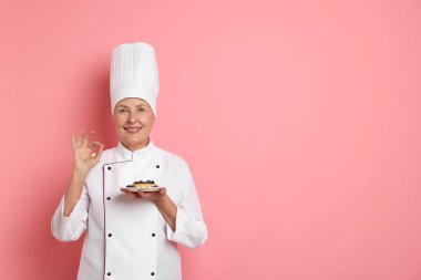 Profesyonel pasta şefi pembe arka planda iyi bir jest gösteriyor. Metin için boşluk