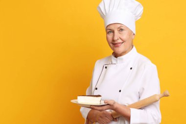 Turuncu arka planda bir parça kek ve oklavayla profesyonel pasta şefi. Metin için boşluk