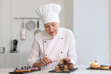 Kıdemli pasta şefi mutfaktaki masada yenilebilir altın yaprak örtüsüyle lezzetli tatlılar hazırlıyor.