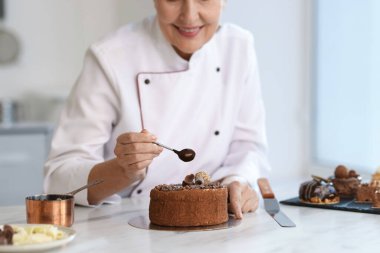 Gülümseyen pasta şefi mutfaktaki masada erimiş çikolatayla süsleme, yakın plan.