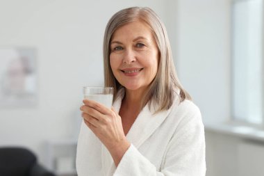 Evde bir bardak kolajen suyu ile gülümseyen kadın.