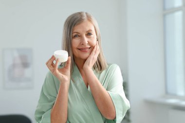 Evde elinde bir kavanoz kolajen kremiyle gülümseyen kadın.