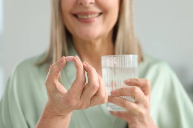 Gri arka planda kolajen hapı ve bir bardak suyla gülümseyen kadın, seçici odaklı.
