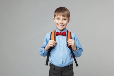 Açık gri arka planda sırt çantası olan sevimli bir okul çocuğu.
