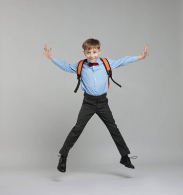 Sırt çantası açık gri arka planda atlayan sevimli okul çocuğu.