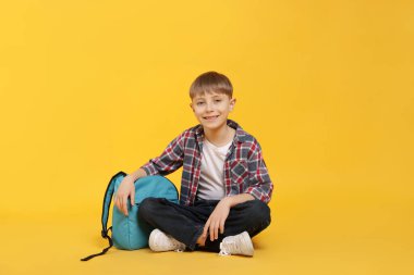Turuncu arka planda sırt çantası olan tatlı bir okul çocuğu.