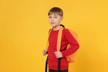 Turuncu arka planda sırt çantası olan tatlı bir okul çocuğu.