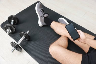 Akıllı telefonlu ve halterli bir adam içeride, manzaranın üstünde.