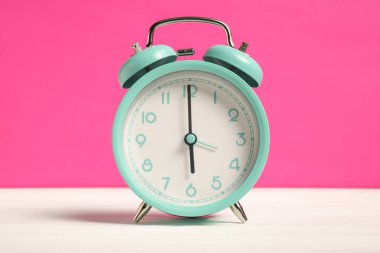Beyaz ahşap masada parlak pembe arka planda bir turkuaz alarm saati.