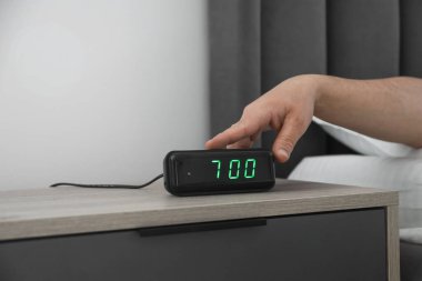 Kapalı bir odada, komodinin üzerindeki dijital çalar saati kapatan adam.