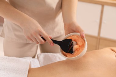 Vücut sargısı için kozmetik ürünler uygulayan estetikçi kaplıca salonundaki kadının sırtına sarıp kapatıyor.