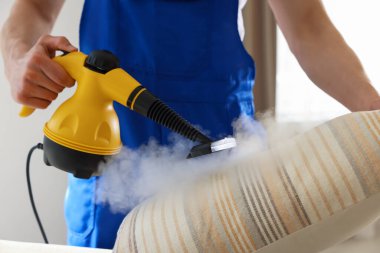 Temizlikçi yastığı evde buhar temizleyicisiyle temizliyor.