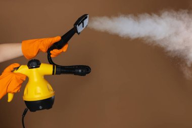 Kahverengi arka planda buhar temizleyicisi olan kadın, yakın plan.