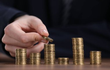 Adam ahşap masadaki para yığınlarına para koyuyor, yakın plan.