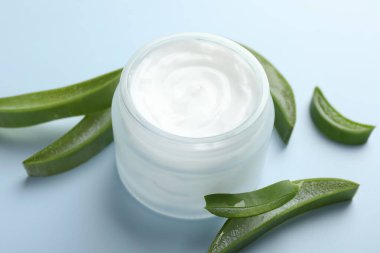 Aloe vera özütüyle nemlendirici krem ve açık mavi arkaplanda yapraklar, yakın plan.
