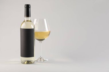 Bardakta lezzetli beyaz şarap ve açık gri arka planda şişe, metin için yer