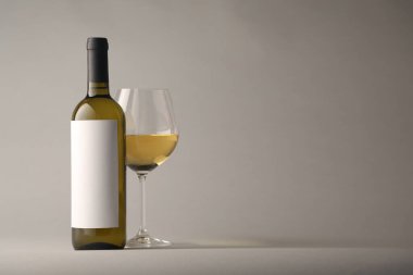 Bardakta lezzetli beyaz şarap ve açık gri arka planda şişe, metin için yer