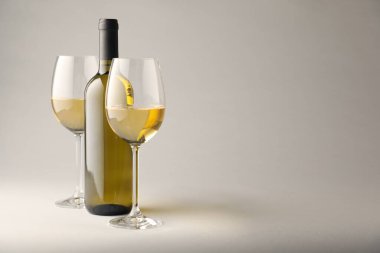 Gözlüklü lezzetli beyaz şarap ve açık gri arka planda şişe, metin için yer