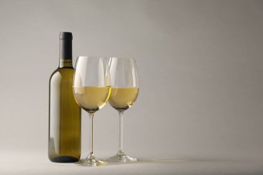 Gözlüklü lezzetli beyaz şarap ve açık gri arka planda şişe, metin için yer