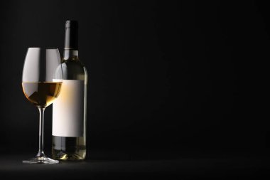 Şarap kadehte ve şişe siyah arka planda, mesaj için yer var.