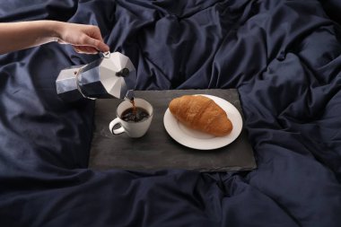 Bir kadın, güzel mavi ipek çarşafları olan bir bardağa kahve dolduruyor.