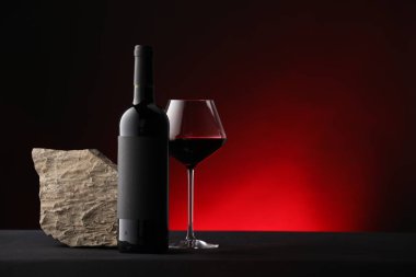 Bir şişe şarap, şarap kadehi ve taş siyah masaya karşı koyu kırmızı arkaplan, metin için boşluk