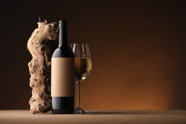 Bir şişe şarap, ağaç kabuğu ve şarap kadehi kahverengi masada, koyu arka planda, metin için yer var.