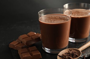 Lezzetli çikolatalı süt, siyah masanın üzerinde talaş ve parçalar, yakın plan.